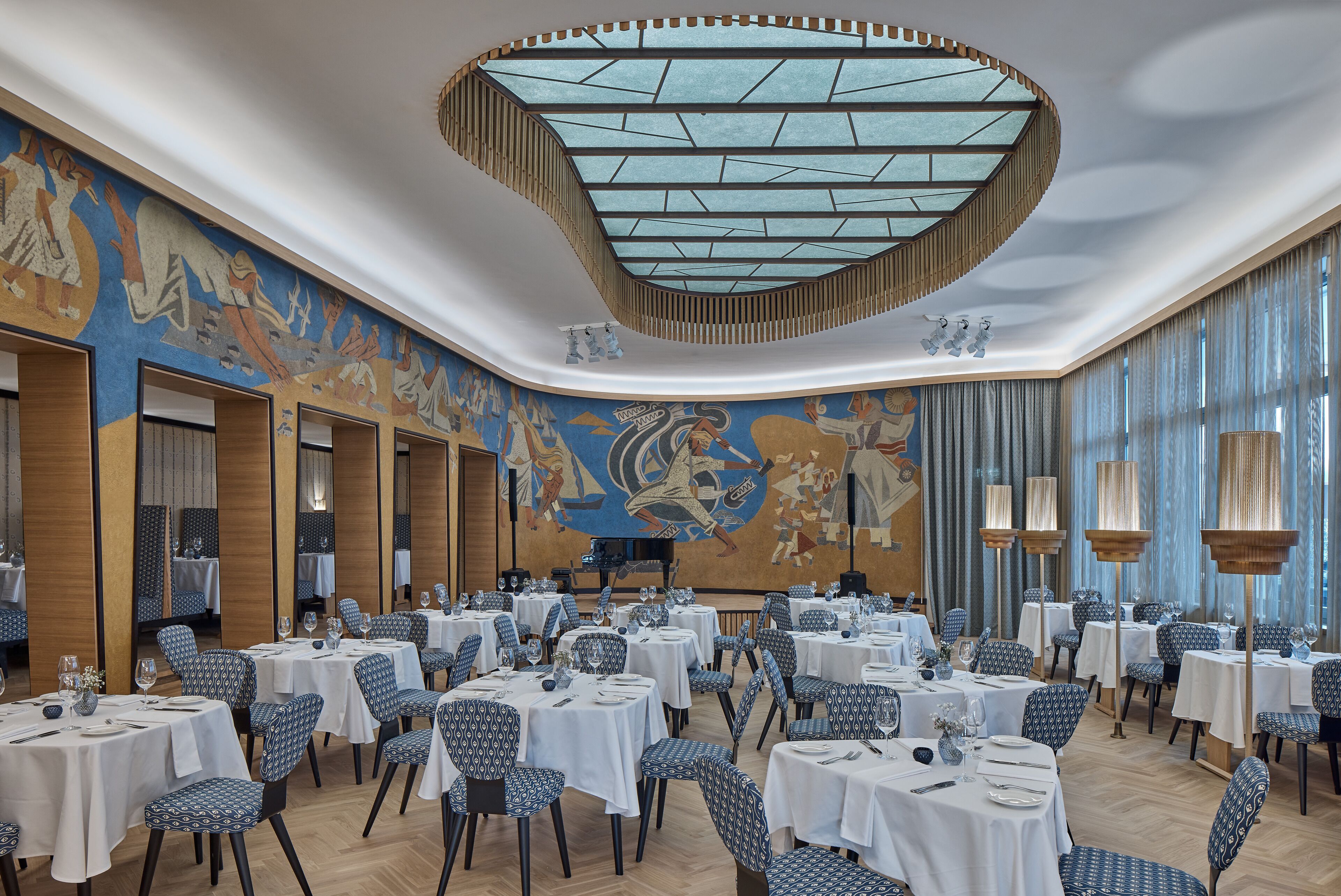 A spacious dining area with multiple tables and chairs, a large mural on the wall, and a unique ceiling design.