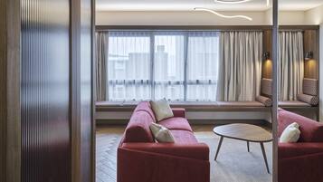 Una habitación de hotel moderna con un sofá rojo, una mesa redonda y un ventanal con cortinas.