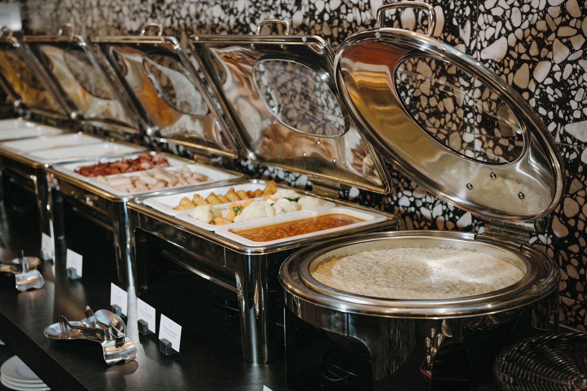 A buffet line with various food items in metal containers, each with a lid.