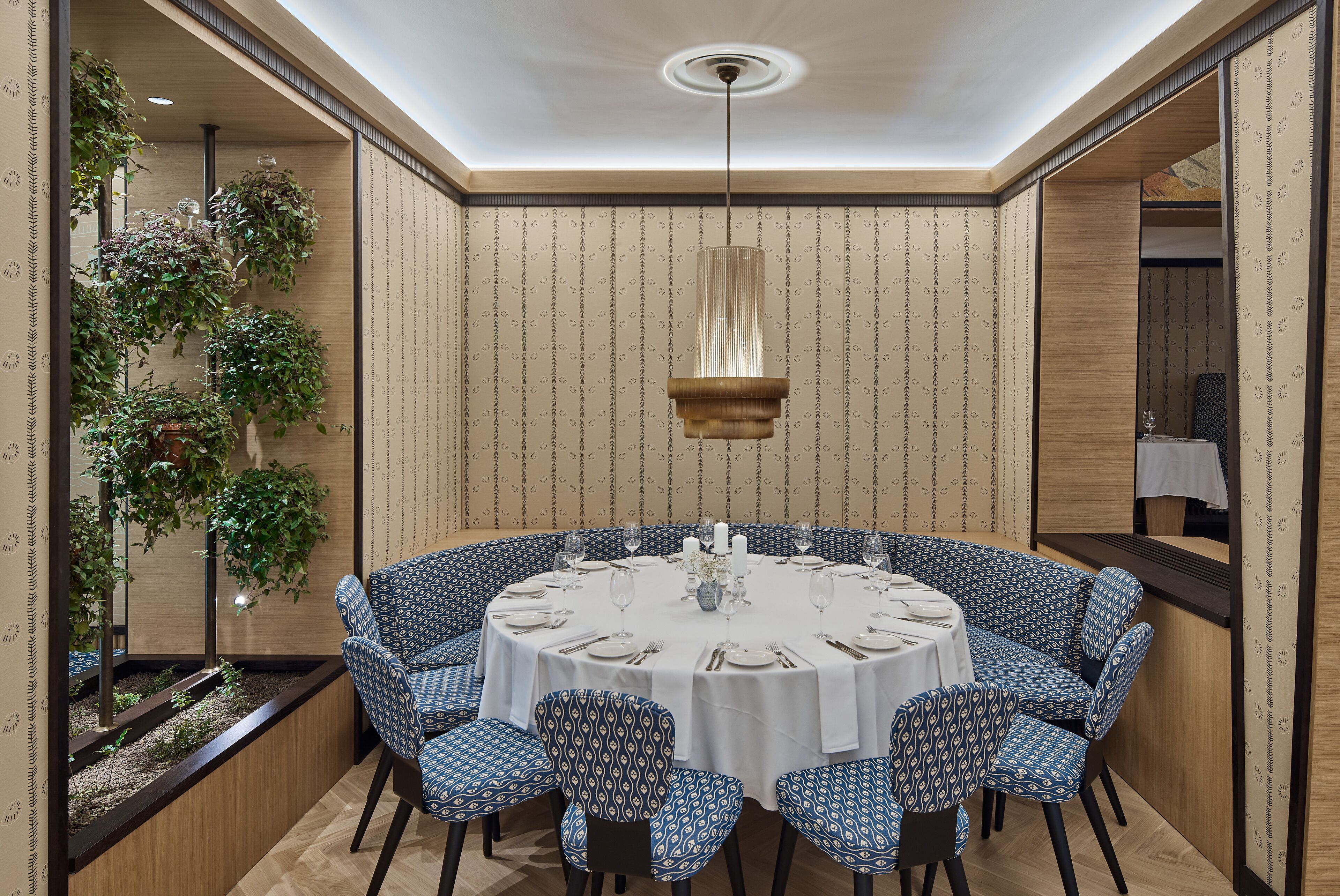 A round dining table with blue patterned chairs, white tablecloth, and a hanging pendant light.