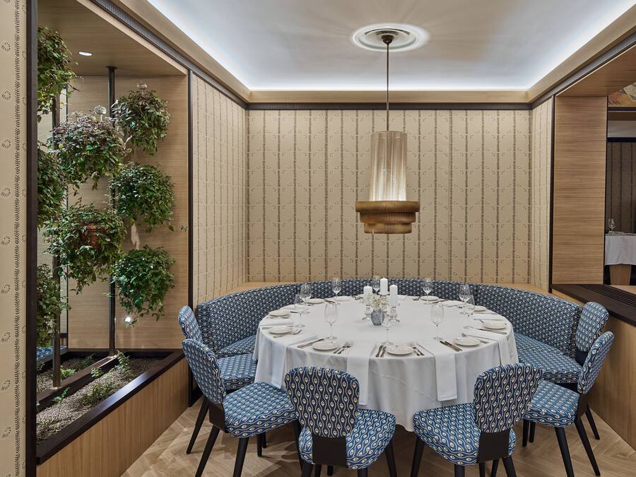 A round dining table with blue patterned chairs, white tablecloth, and a hanging pendant light.