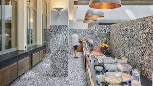 A modern kitchen with a marble backsplash, a long counter with various food items, and pendant lighting.