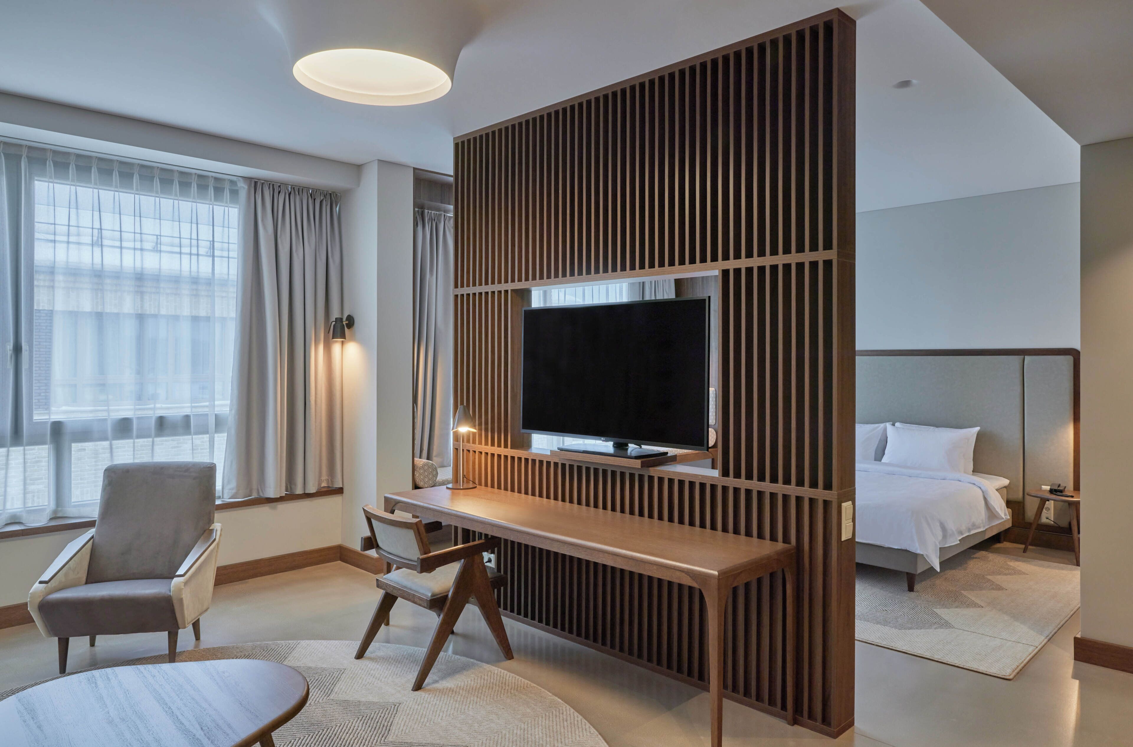 A hotel room with a TV, a desk, a chair, a bed, and a window with curtains.