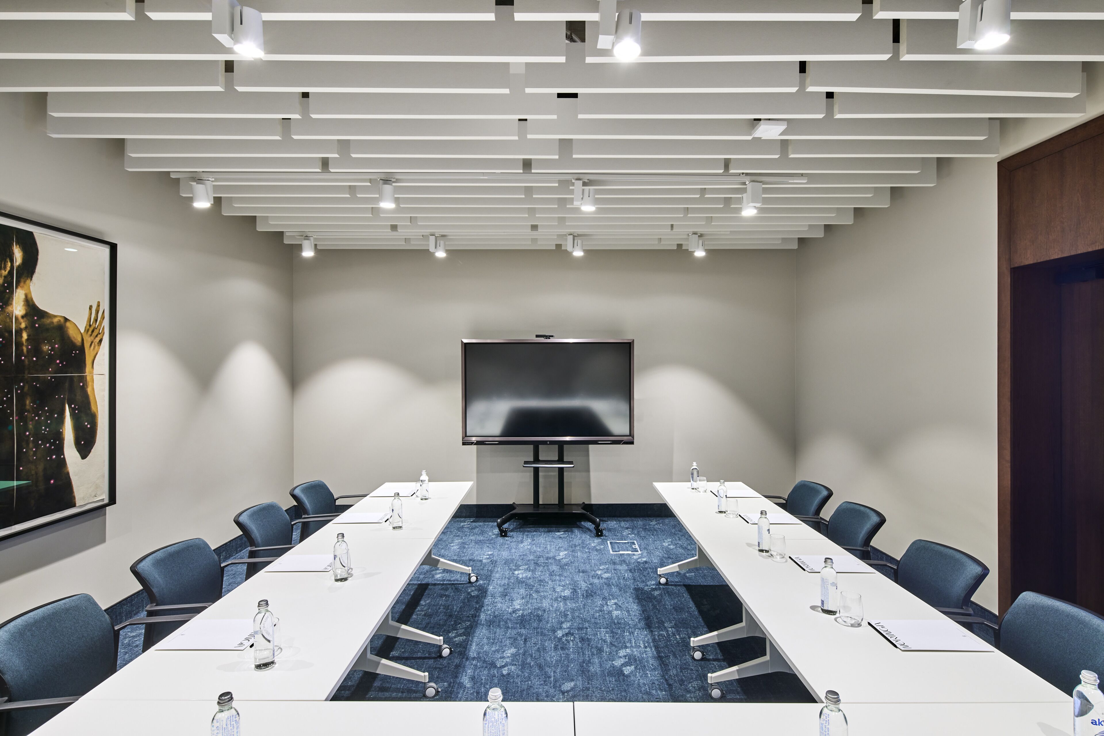 A conference room with a long table, chairs, a projector screen, and a blue carpet.
