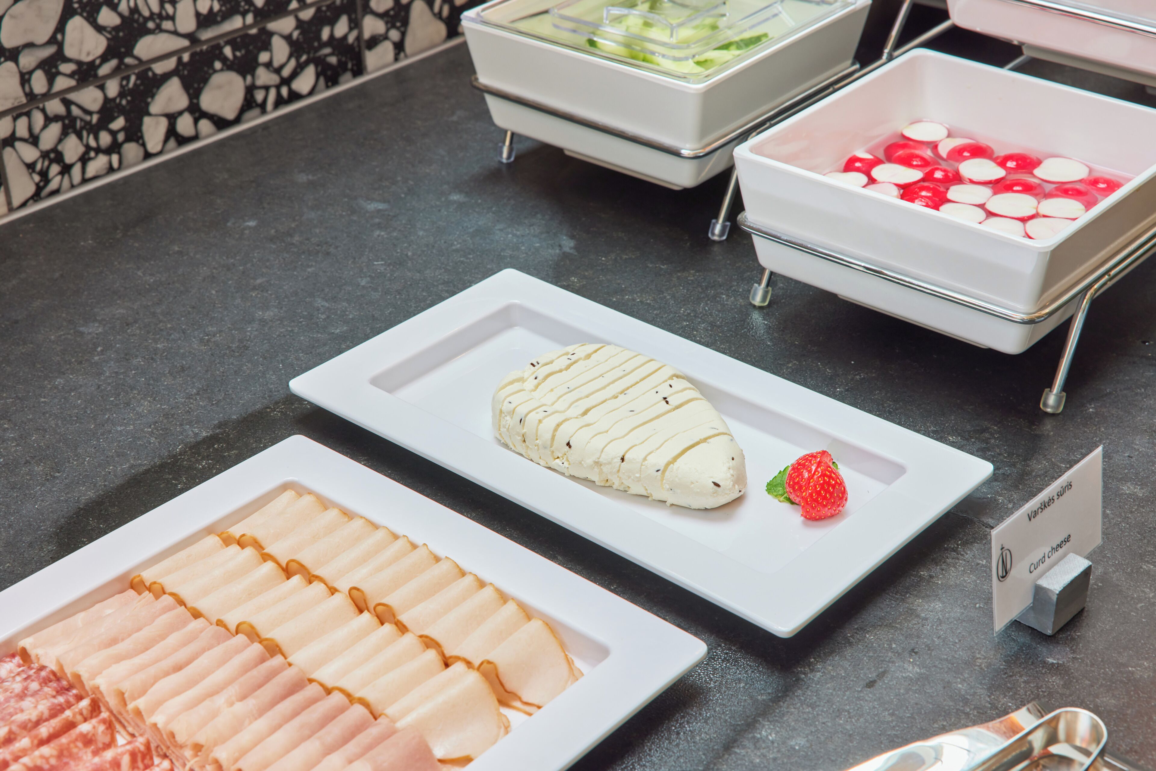 Un bufé con diversos alimentos, incluyendo un plato de queso blanco, una fresa y un recipiente etiquetado 'Varik's curd cheese'.