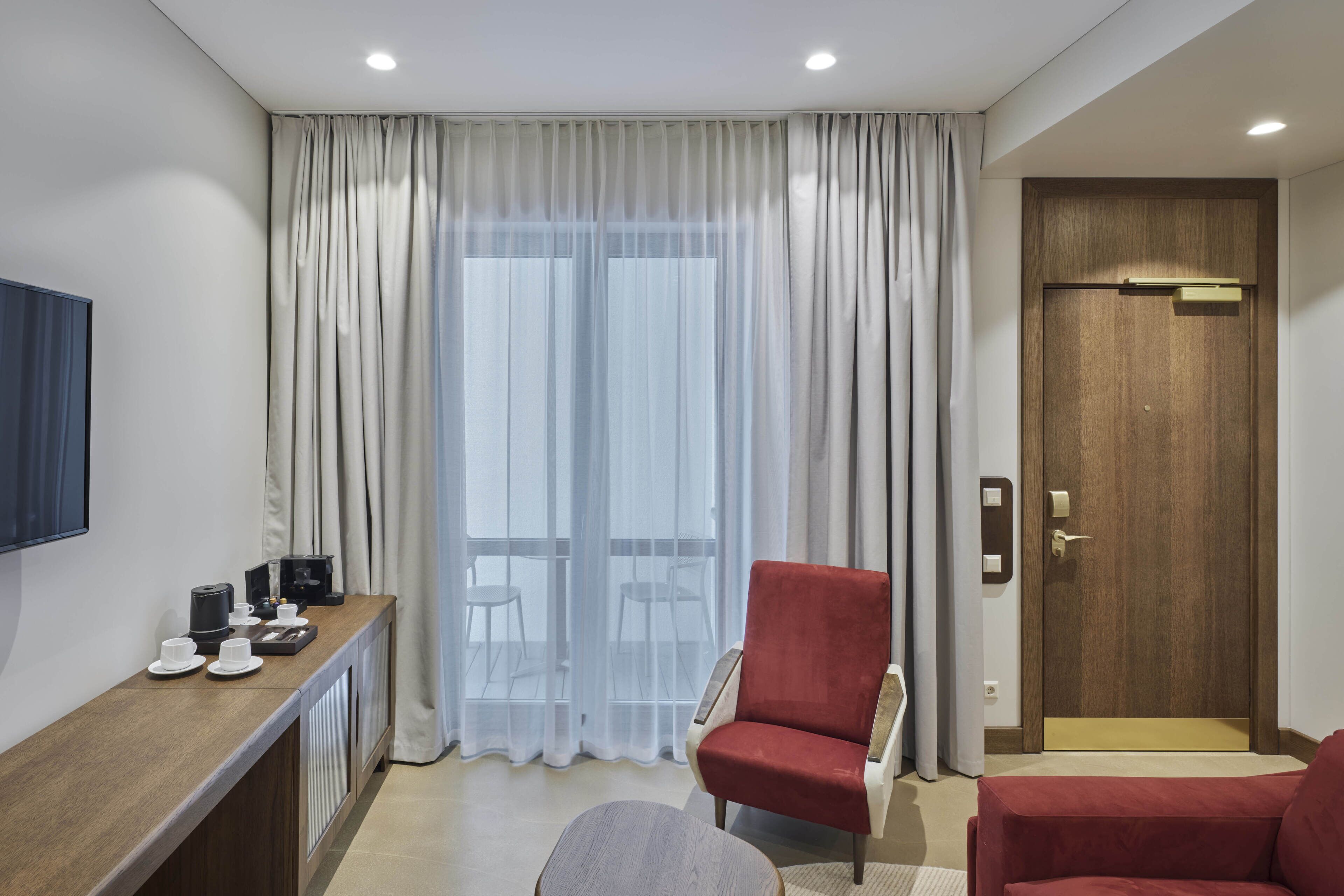 Une chambre d’hôtel avec un bureau en bois, un fauteuil rouge, un canapé et une porte dotée d’une poignée.