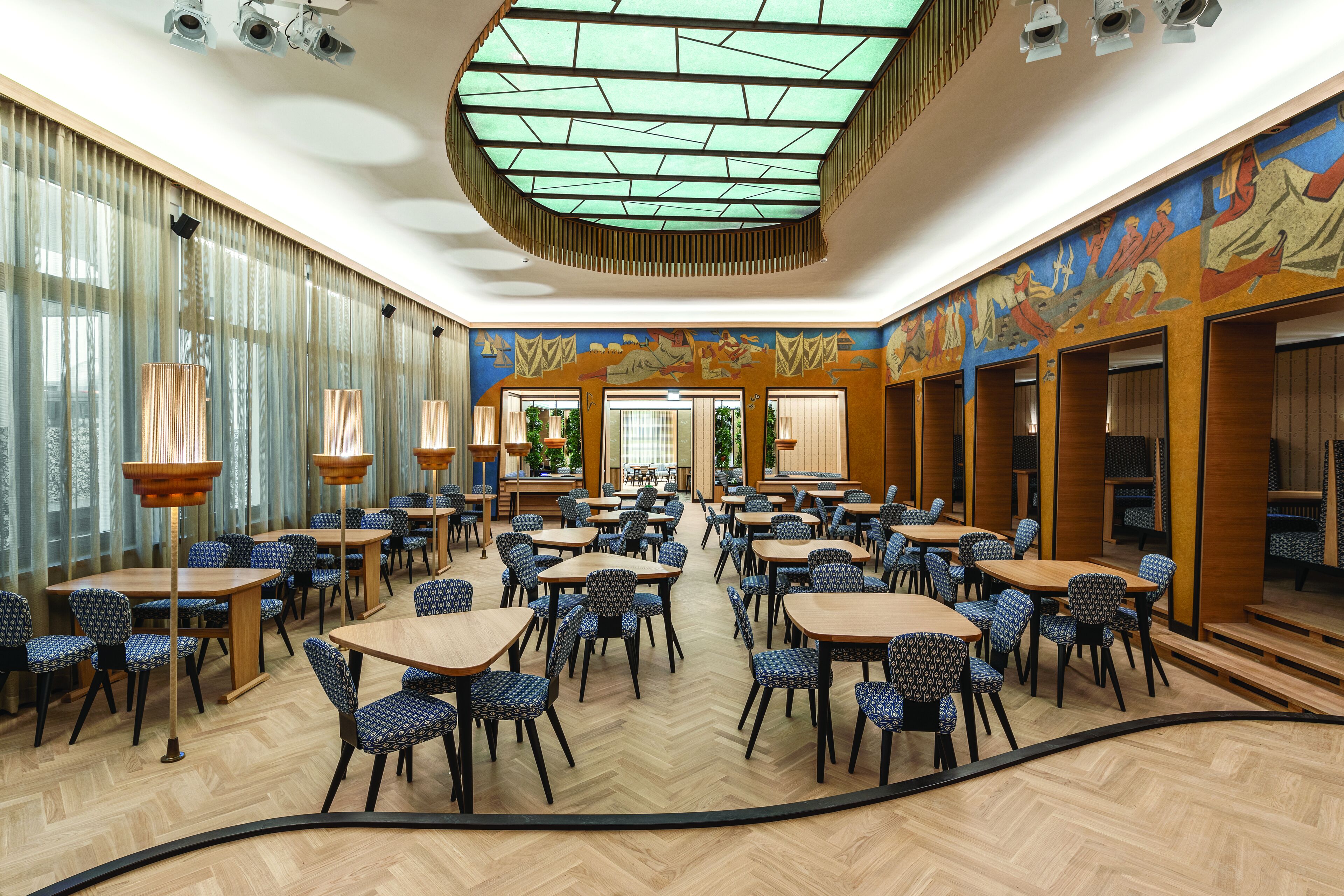 A spacious dining area with multiple tables and chairs, a patterned floor, and a large mural on the wall.