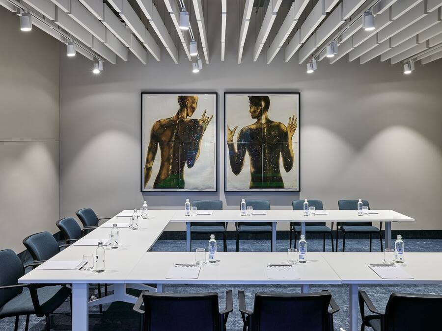 Une salle de conférence avec une longue table, des chaises et deux grandes peintures au mur.