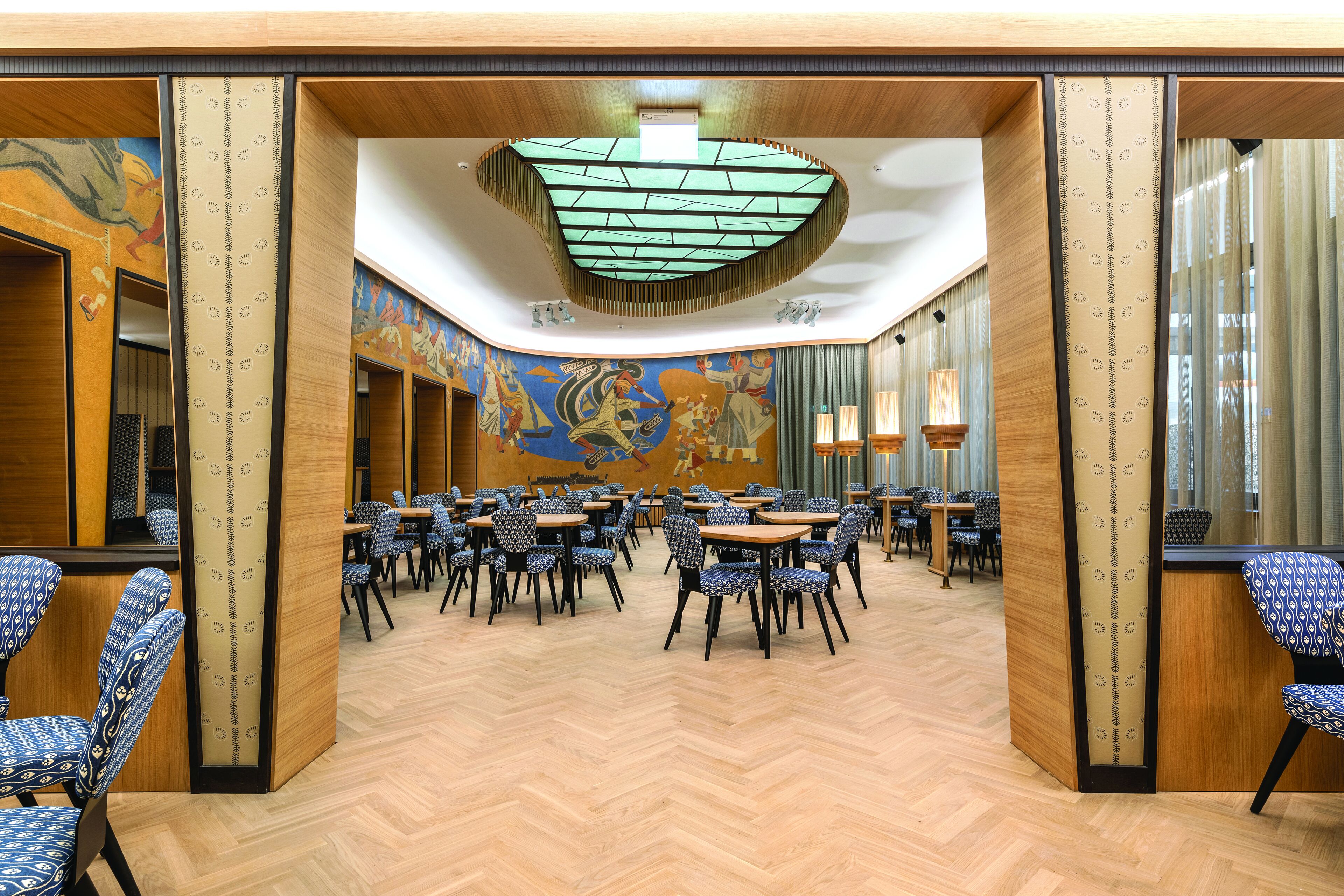 Un vaste espace dédié à la salle à manger, avec de hauts plafonds, des chaises à motifs et une grande fresque murale.