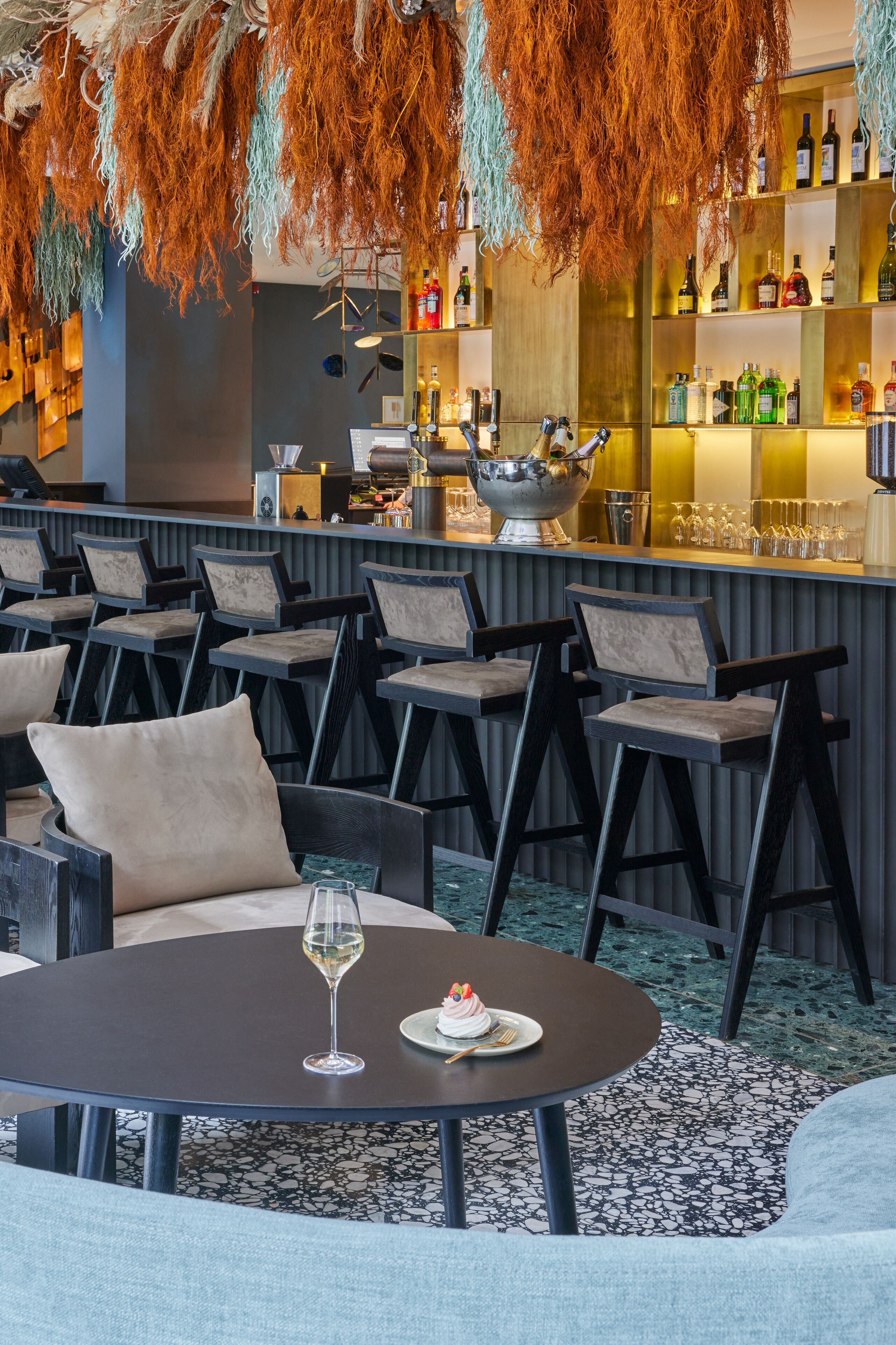 A bar area with multiple seating options, a bar counter with various bottles, and a decorative hanging element.