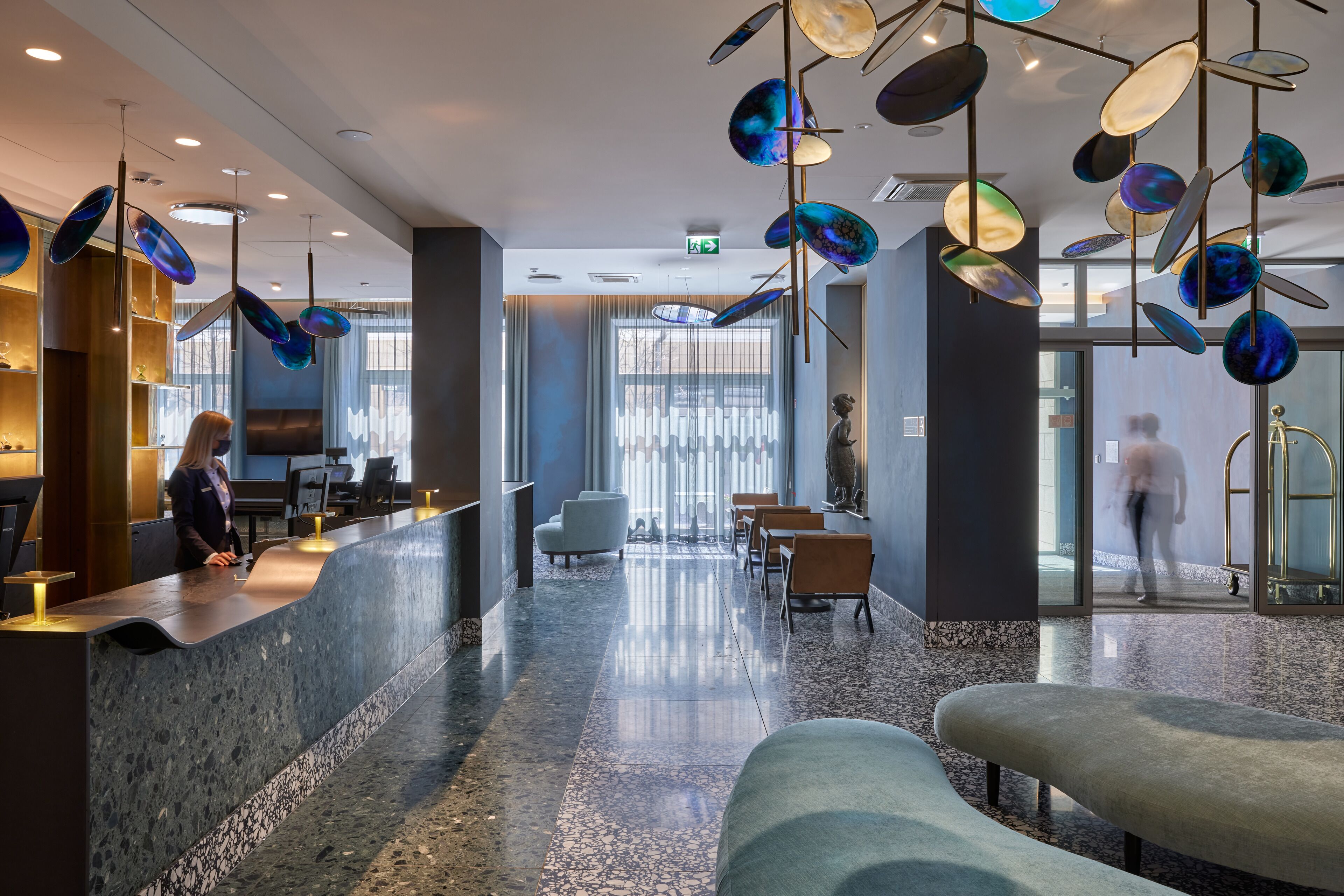 A modern hotel lobby with a reception desk, seating area, and decorative hanging elements.