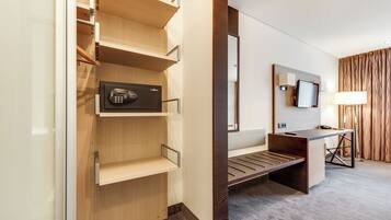 A hotel room with a wooden wardrobe, a desk with a television, and a lamp.