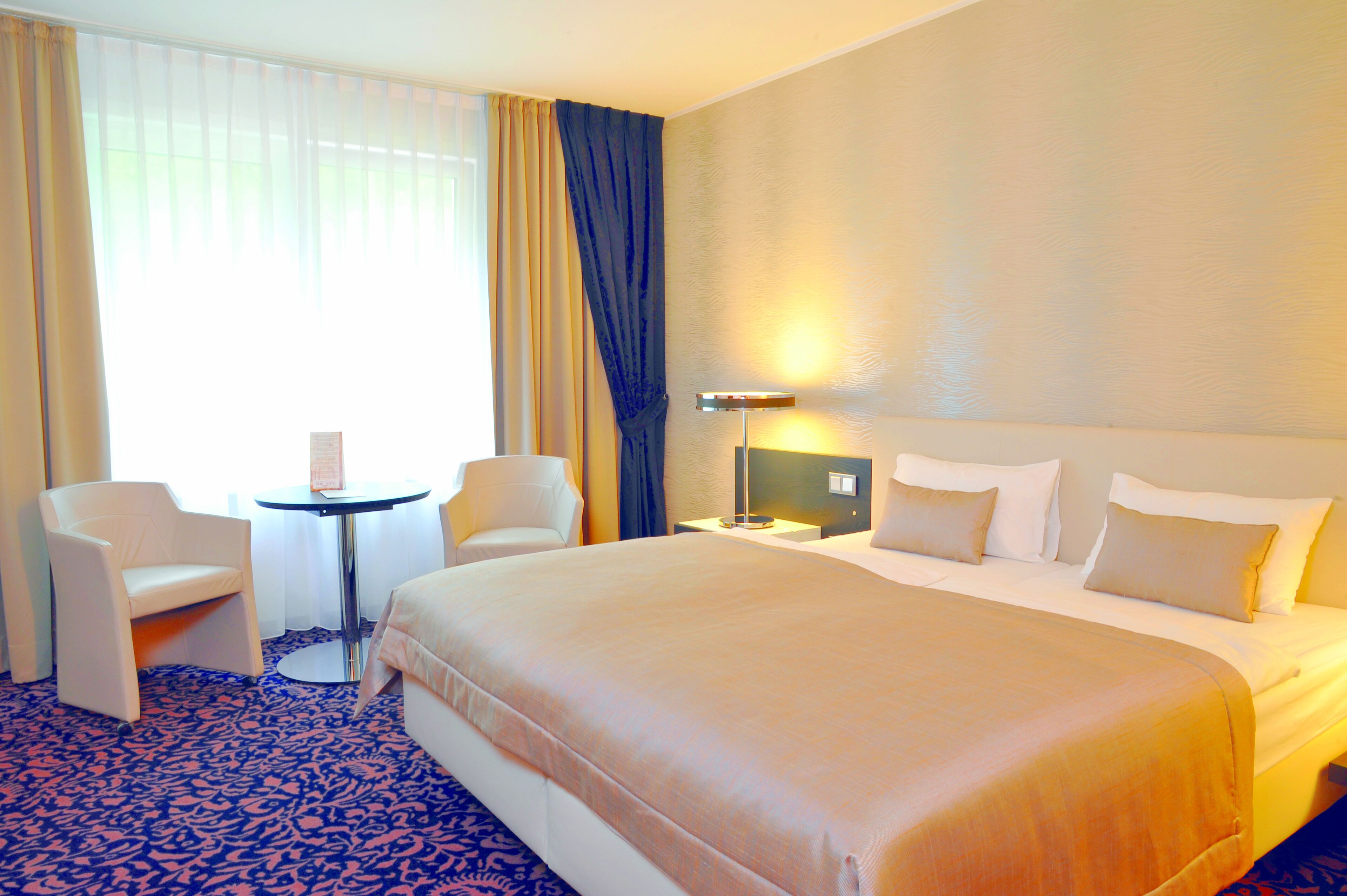 A hotel room with a large bed, two chairs, a small table, and a lamp.