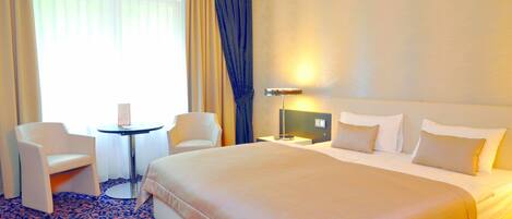 A hotel room with a large bed, two chairs, a small table, and a lamp.