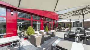 An outdoor patio area with wicker furniture, tables, and umbrellas. - Parc Hotel Alvisse (Luxembourg City)