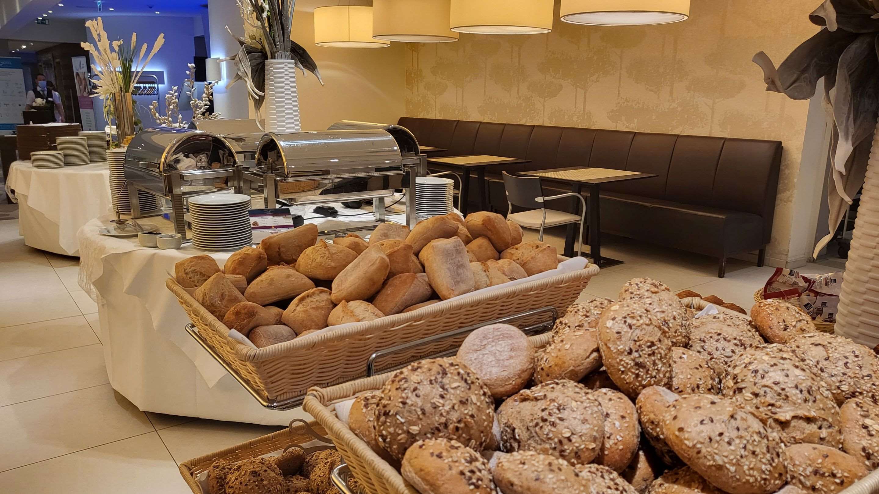 Zona de buffet con panes y pasteles diversos, estación de buffet con platos y cubiertos, y  área de estar con mesas y sillas.