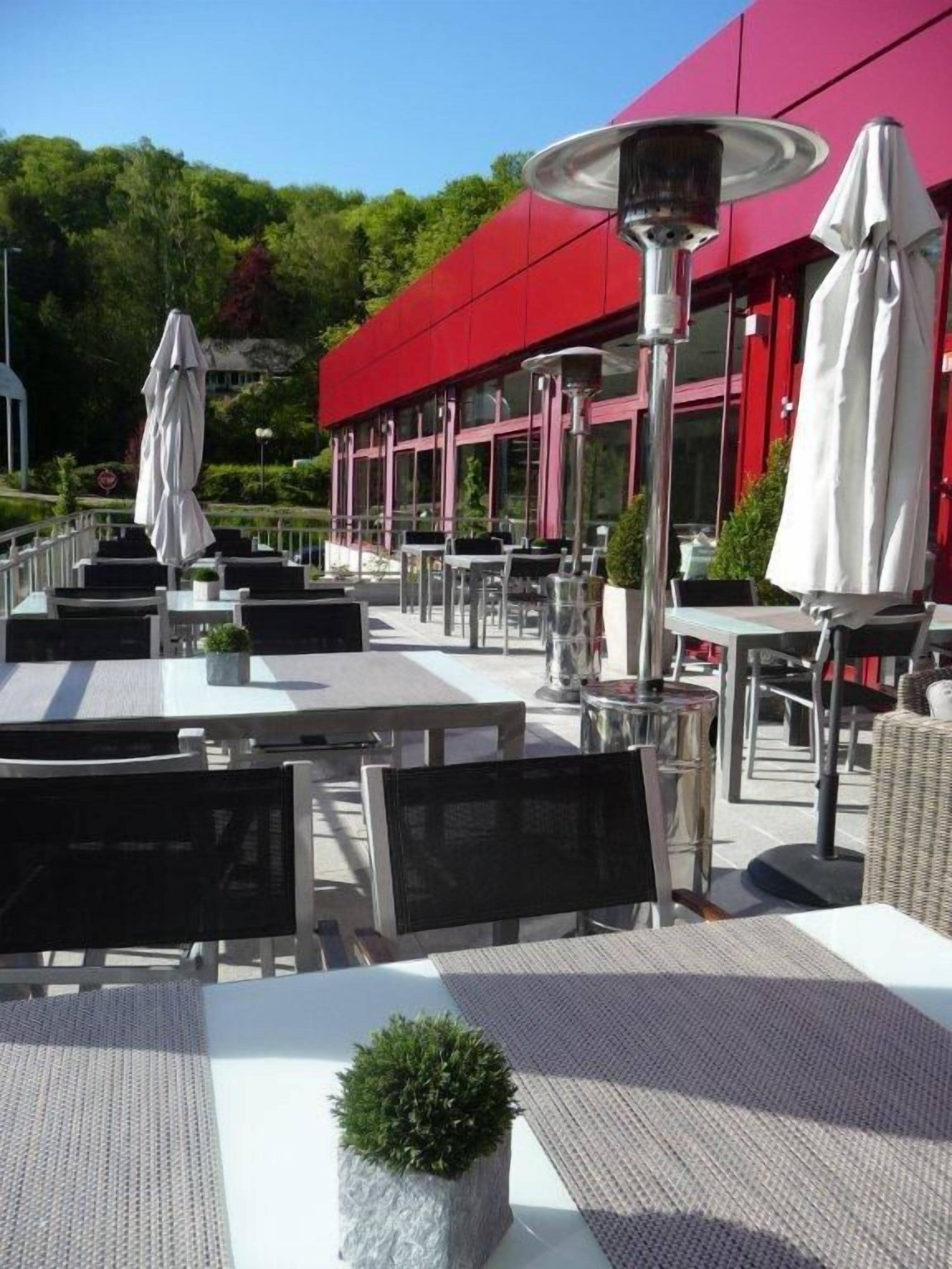 An outdoor seating area with tables and chairs, umbrellas, and a red building in the background.