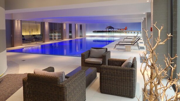 A modern indoor pool area with lounge chairs and a glass wall overlooking the pool. - Parc Hotel Alvisse (Luxembourg City)
