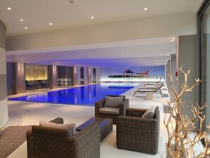 A modern indoor pool area with lounge chairs and a glass wall overlooking the pool. - Parc Hotel Alvisse (Luxembourg City)
