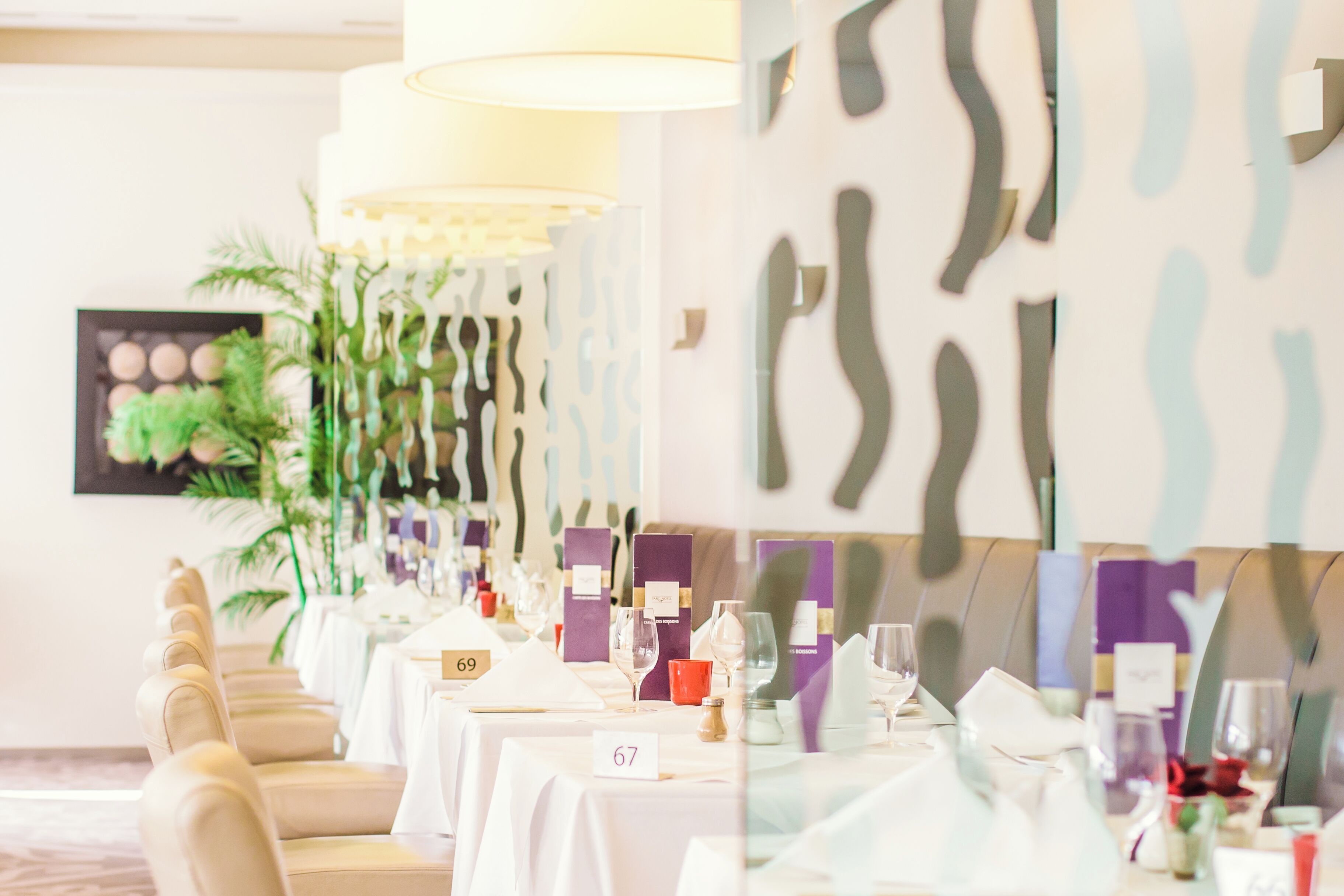 Une salle de banquet avec des tables numérotées 67 et 69, des nappes blanches et une grande plante en arrière-plan.
