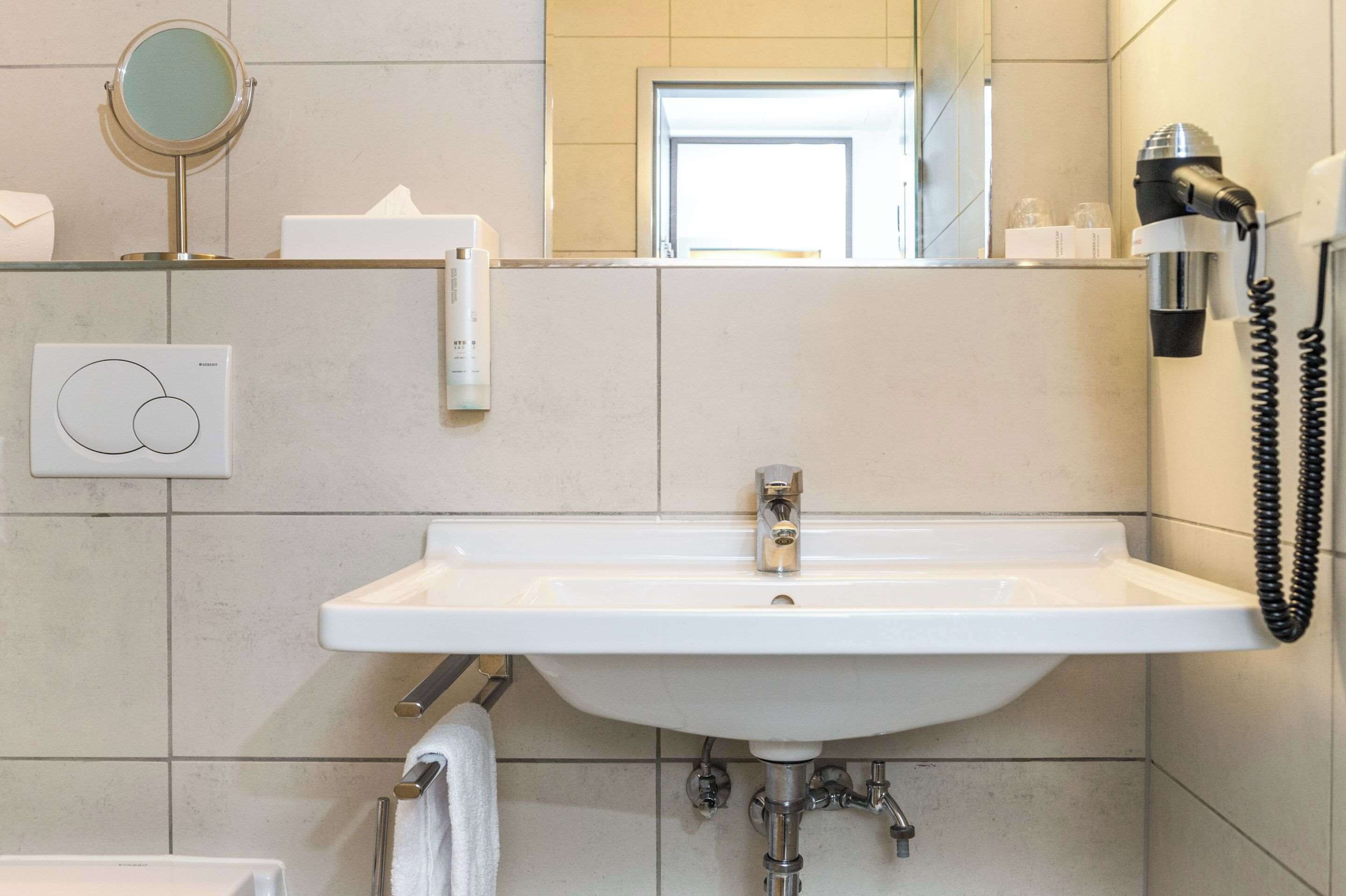 Un bany amb un lavabo blanc, un mirall, un assecador d'eixugat i una barra de tovalloles.