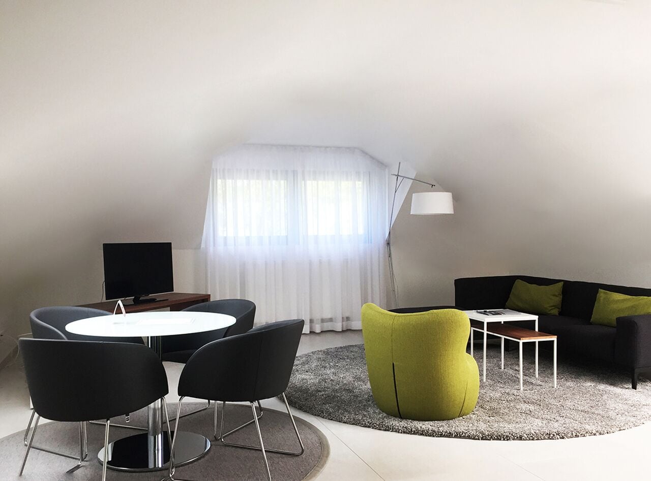 Ein modernes Wohnzimmer mit einem runden Tisch, schwarzen und grünen Stühlen, einer Couch und einem Fernseher.