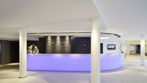 A modern hotel reception area with a curved reception desk, a clock, and a floral arrangement. - Parc Hotel Alvisse (Luxembourg City)