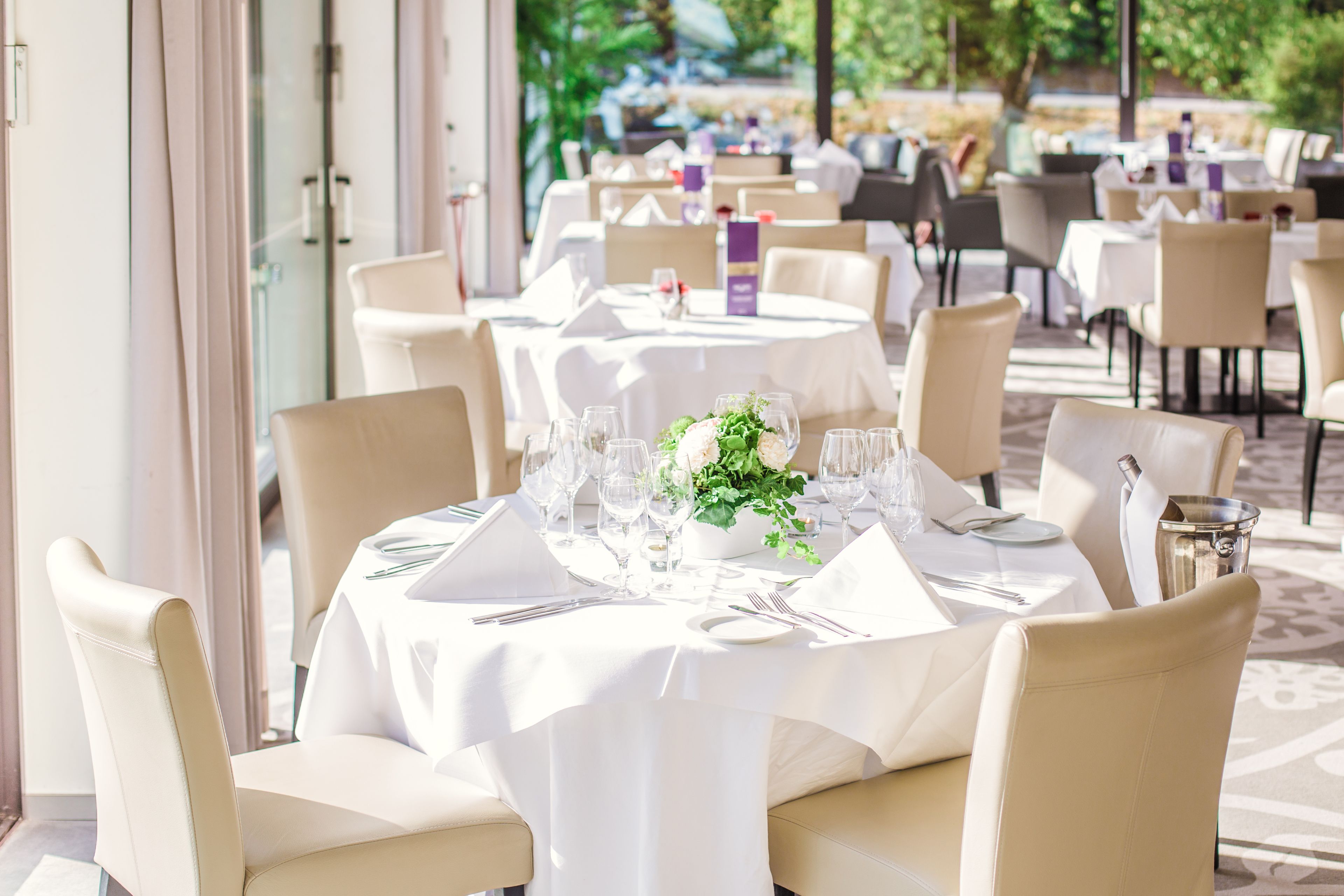 Ein Restaurant mit runden Tischen, gedeckt für das Essen, mit weißen Tischdecken und Stühlen.
