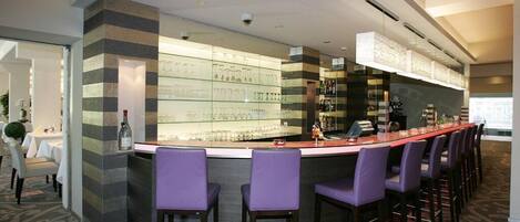 Una zona de bar con una barra curva, varios taburetes y una vitrina de vidrio llena de botellas.