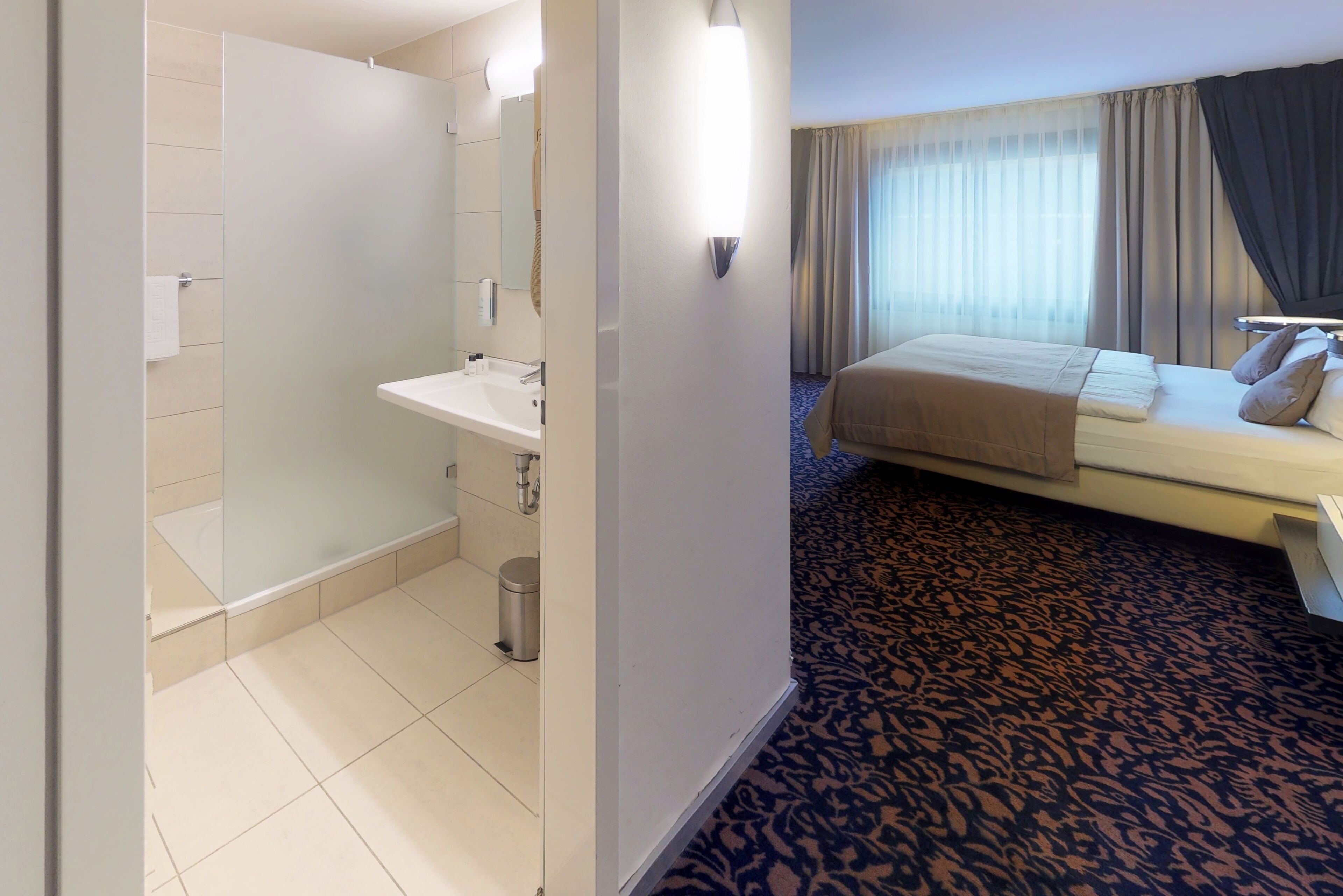 Habitación de hotel con baño, cama y alfombra estampada.