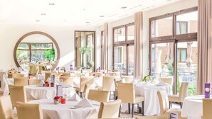 A spacious dining area with multiple tables and chairs, large windows, and a view of greenery outside. - Parc Hotel Alvisse (Luxembourg City)