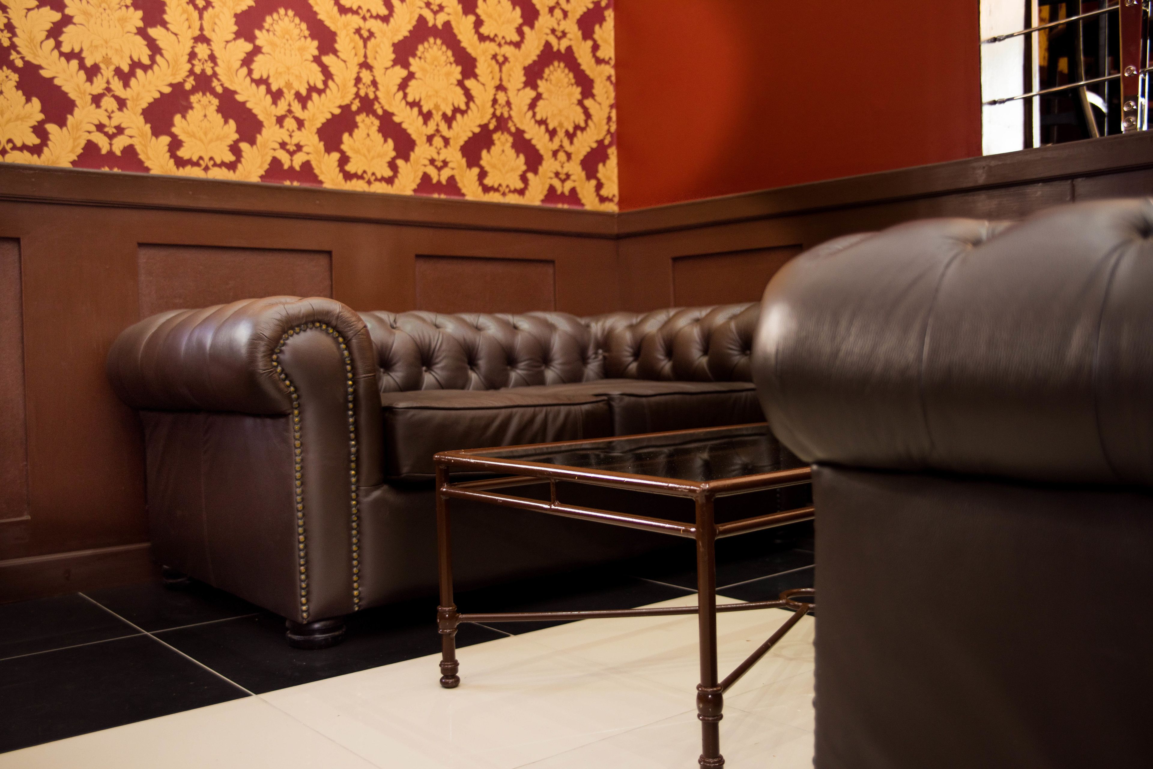 Un canapé en cuir marron, accompagné d’une table basse à structure métallique, se trouve dans une pièce dont les murs sont recouverts d’un papier peint à motifs et d’un lambris en bois.