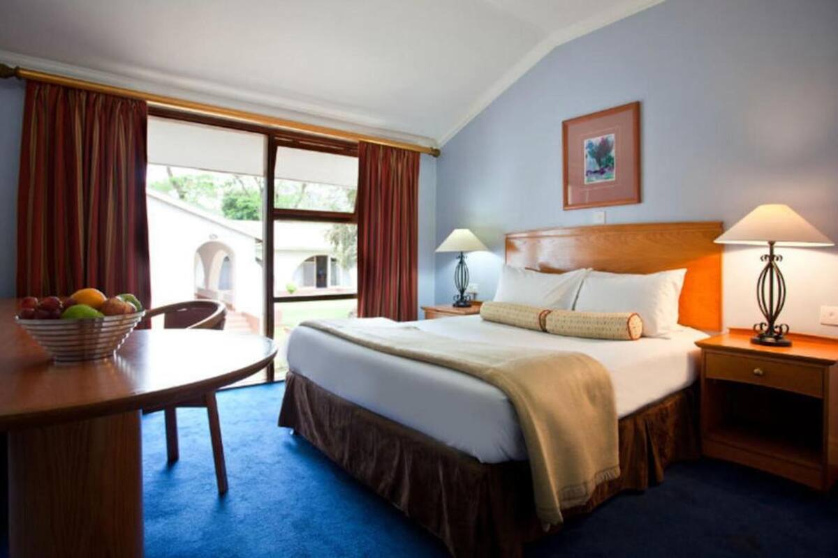 A hotel room with a bed, two bedside tables with lamps, a chair, a desk with a fruit bowl, and a window with curtains.