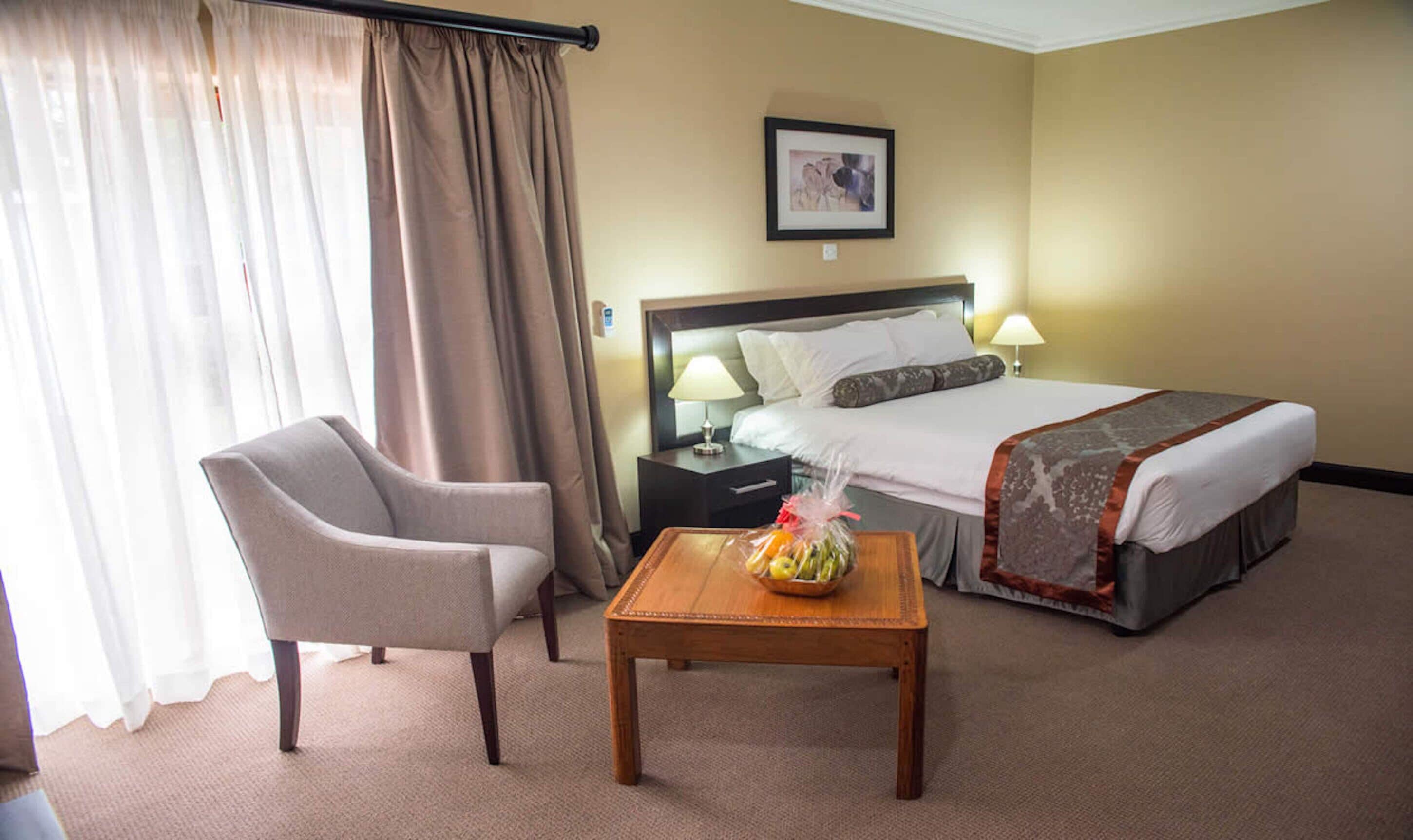 Una habitación de hotel con cama, una silla, una mesita de noche, una lámpara y una mesa con fruta.