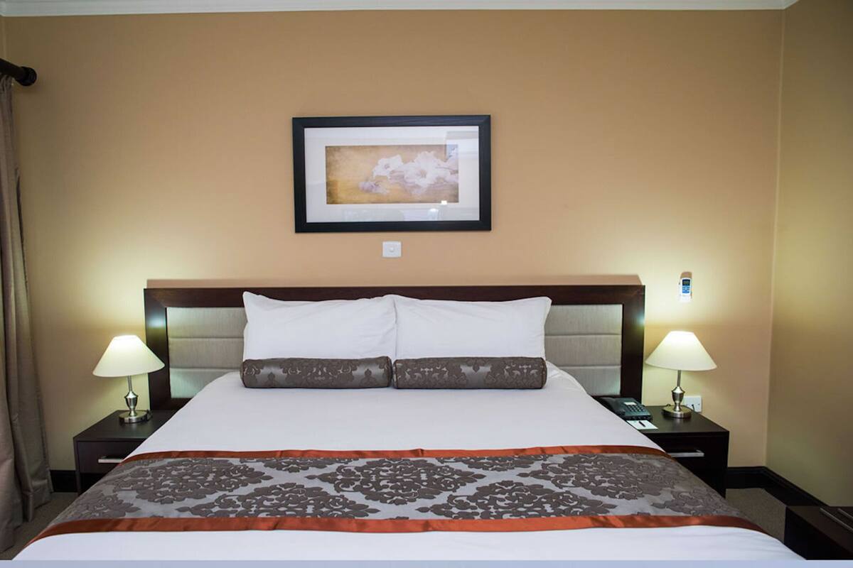 A hotel room with a large bed, two bedside tables, a framed picture on the wall, and a curtain on the window.
