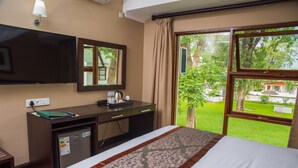 A hotel room with a bed, a desk, a TV, and a window with a view of a garden. - Sunbird Lilongwe (Lilongwe)