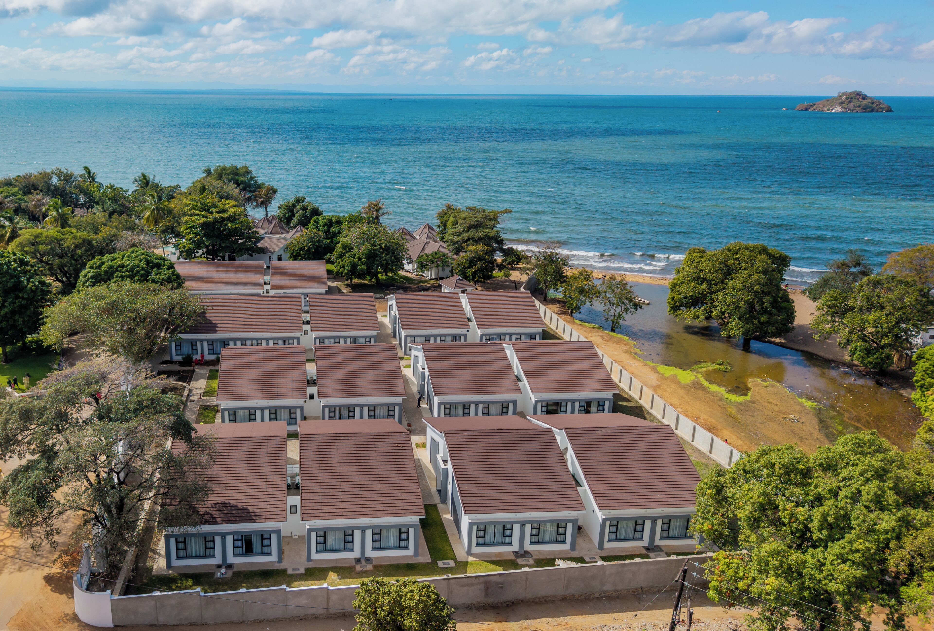 Um hotel à beira-mar com edifícios de vários andares, vista para a praia e uma pequena ilha ao longe.