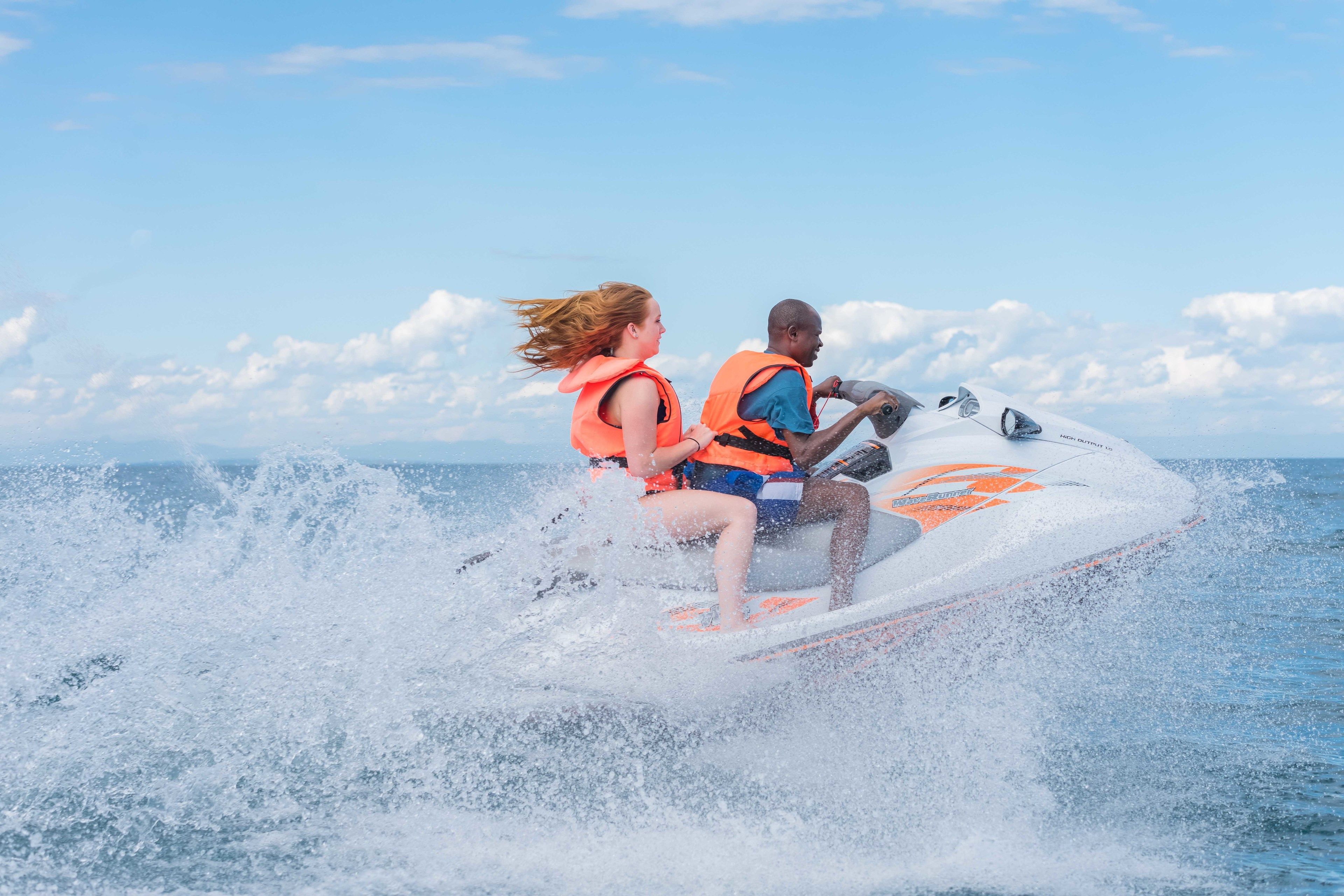 Dos personas en un jet ski, usando chalecos salvavidas.