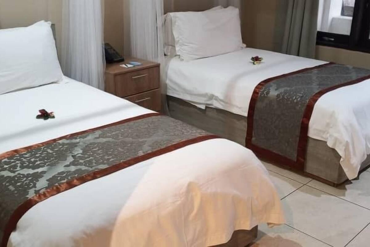 Two twin beds with white linens and decorative headboards, a bedside table with a lamp, and a window with curtains.