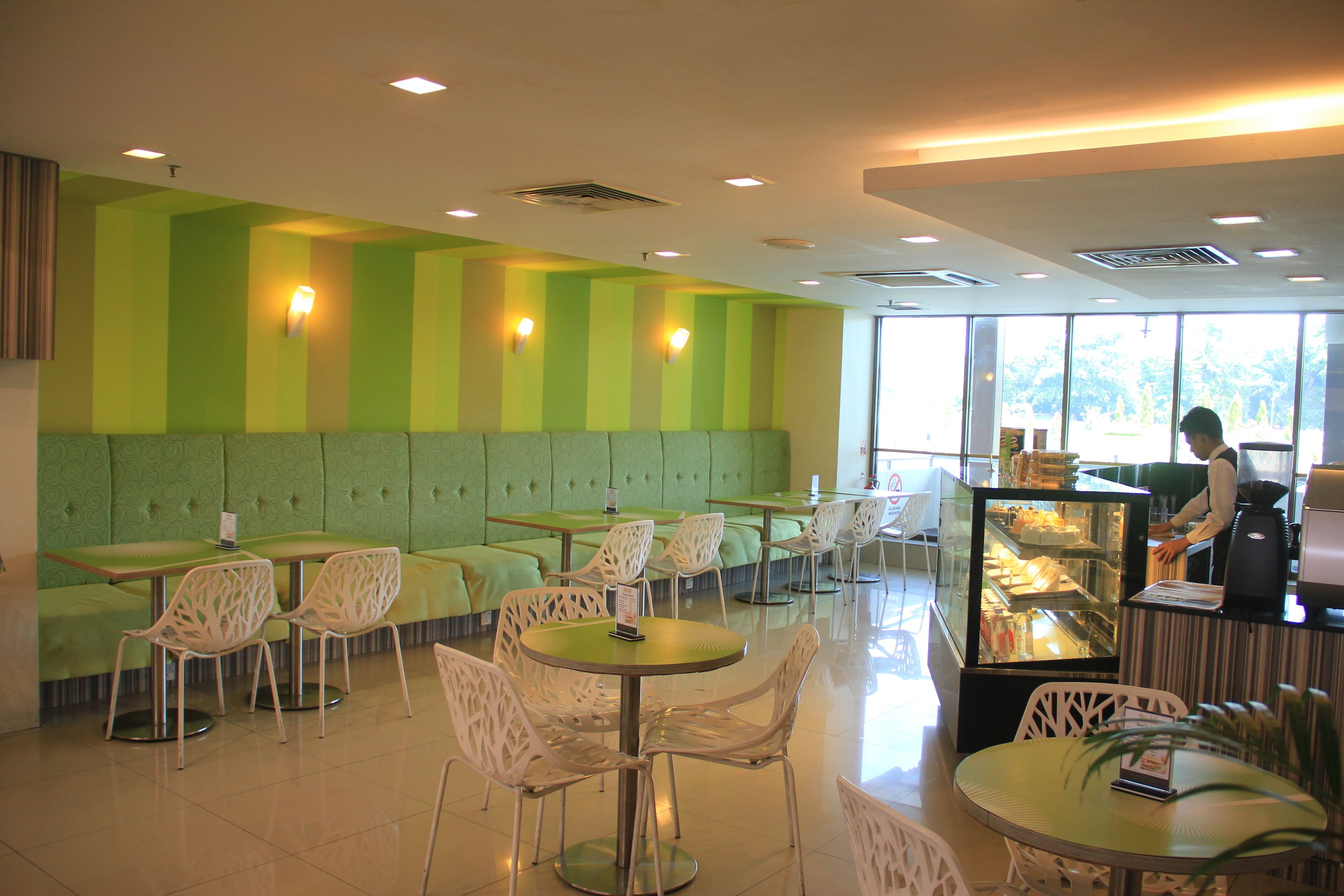 A restaurant with green upholstered booths and white chairs, a coffee machine, and a display case with food.