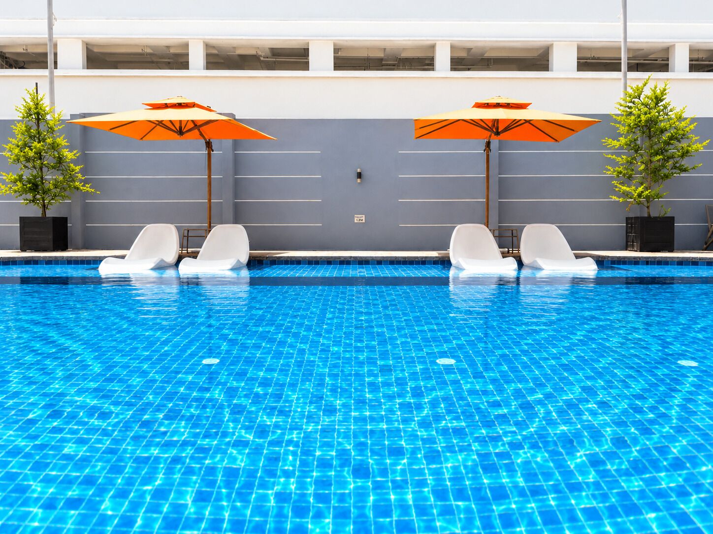 A swimming pool with blue tiles, white lounge chairs, and orange umbrellas.