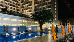 Una piscina con sillones de playa y sombrillas, rodeada por un edificio con varios balcones.