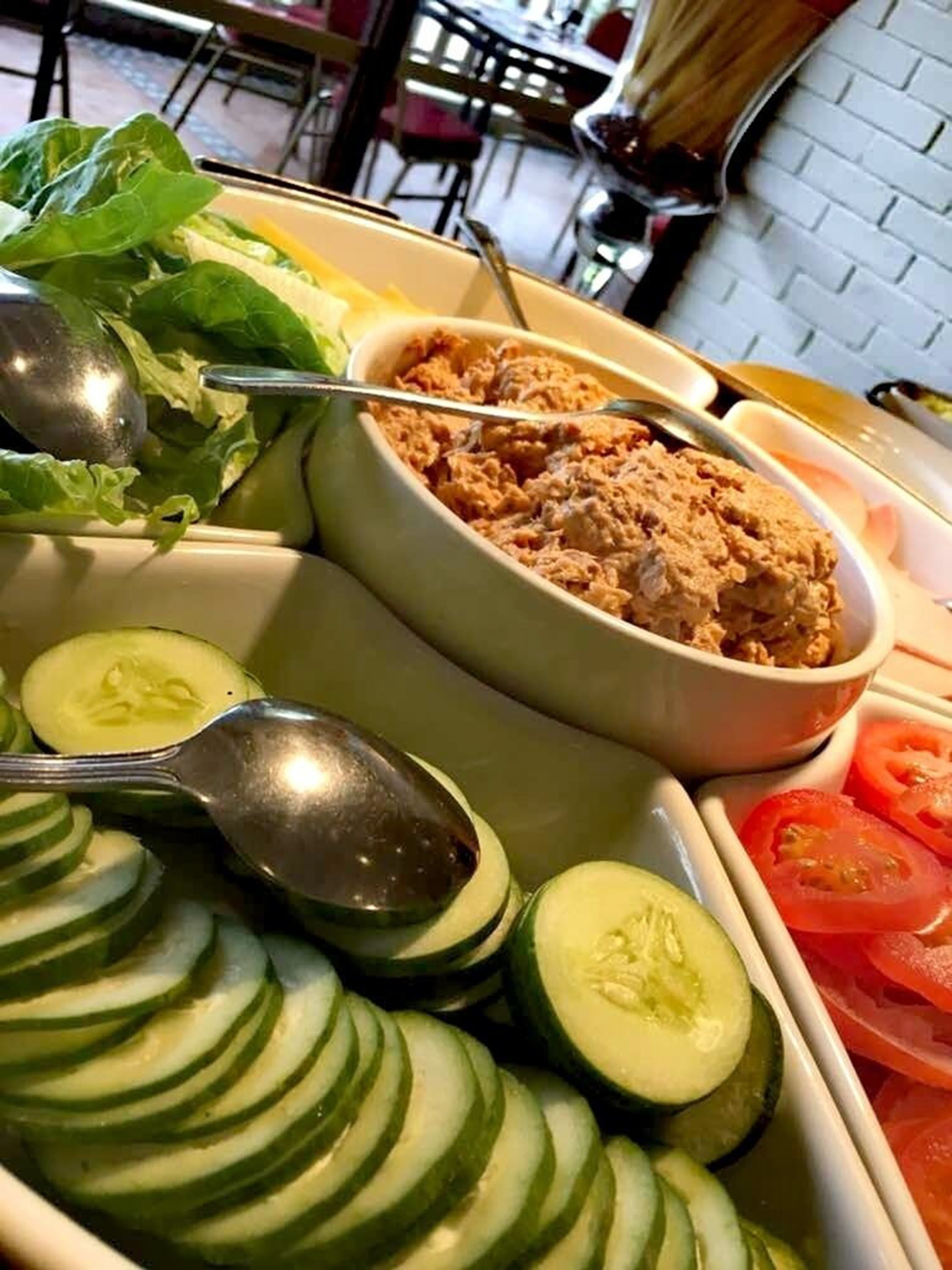 A meal tray with sliced cucumbers, tomatoes, and a bowl of food, possibly a salad or dip, in a restaurant setting.
