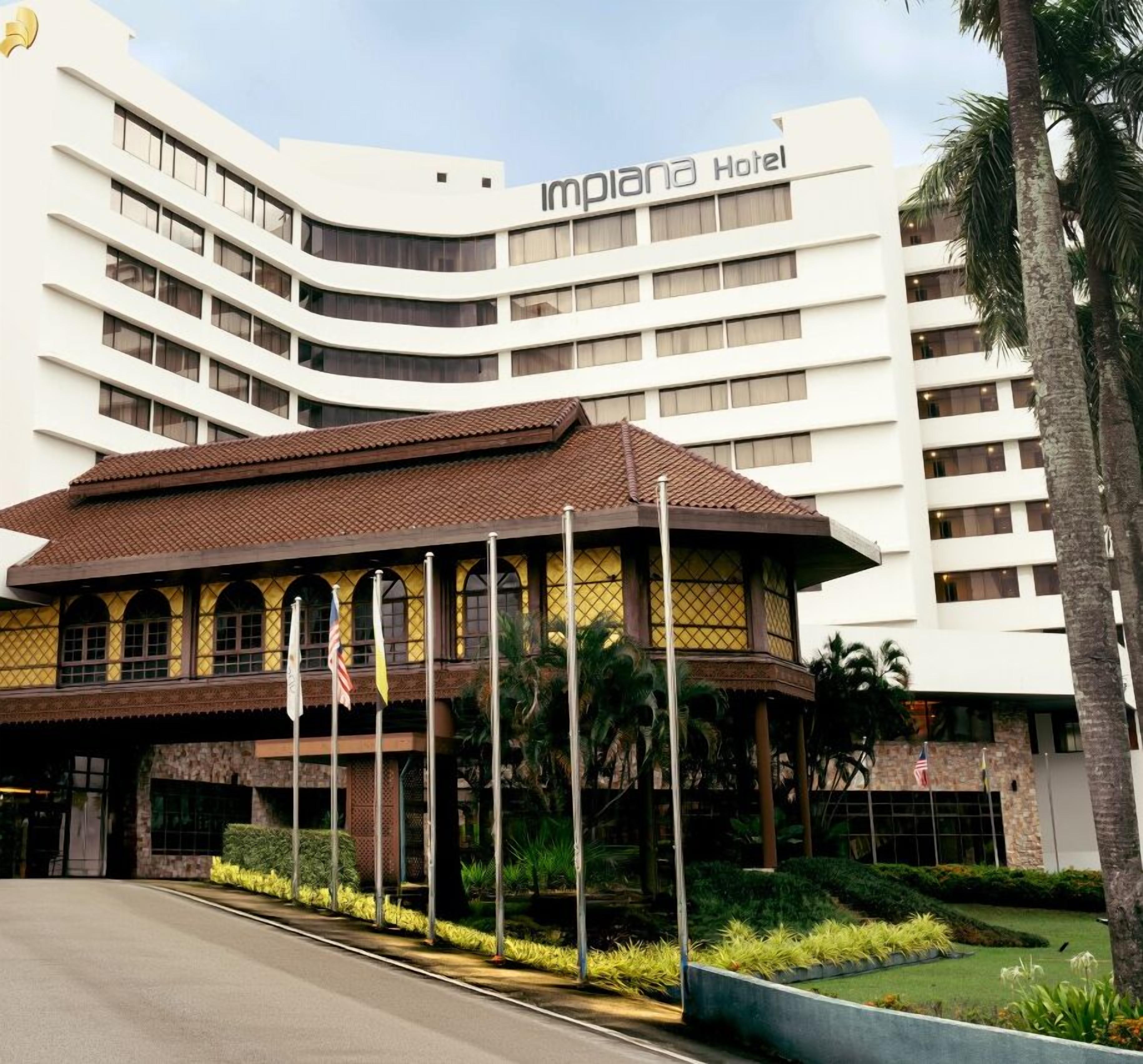 Un moderno edificio hotelero con fachada curva, una entrada cubierta con arcos y una zona de jardín bien cuidada.