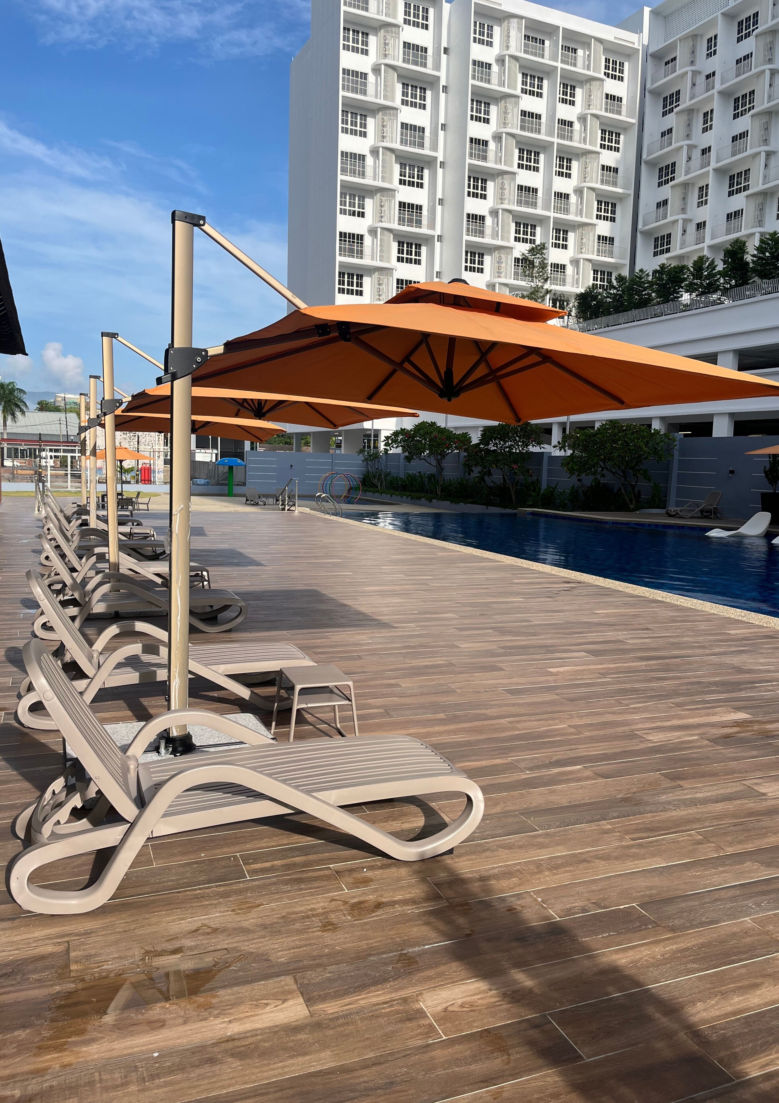 A poolside area with lounge chairs and umbrellas, a pool, and a building in the background.