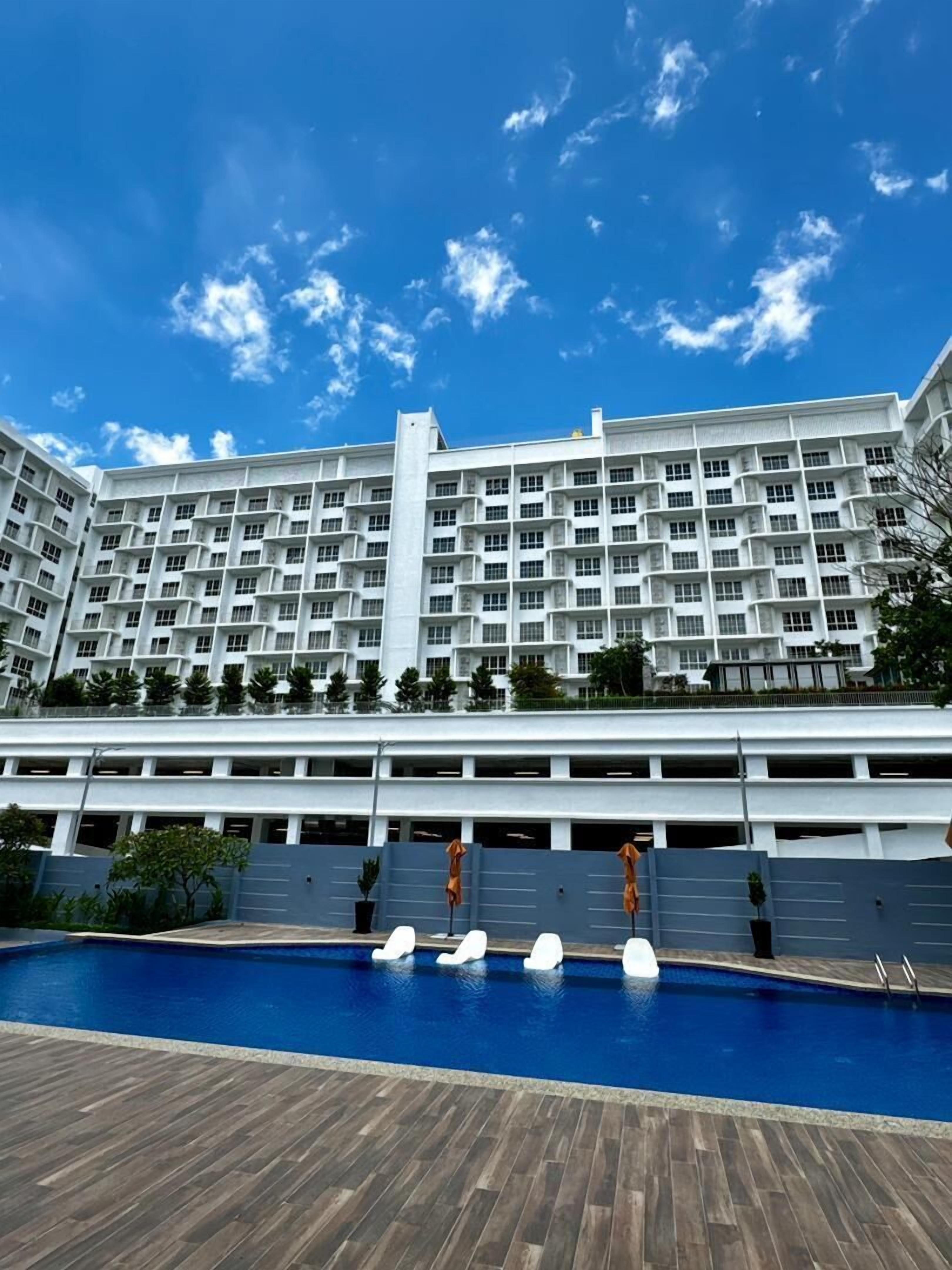 A hotel with multiple floors, a swimming pool, and a clear blue sky.