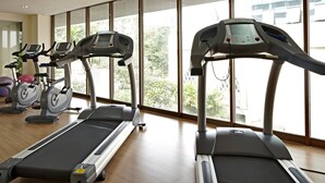 Un gimnasio con cintas de correr y bicicletas estáticas, ventanas amplias y suelo de madera.