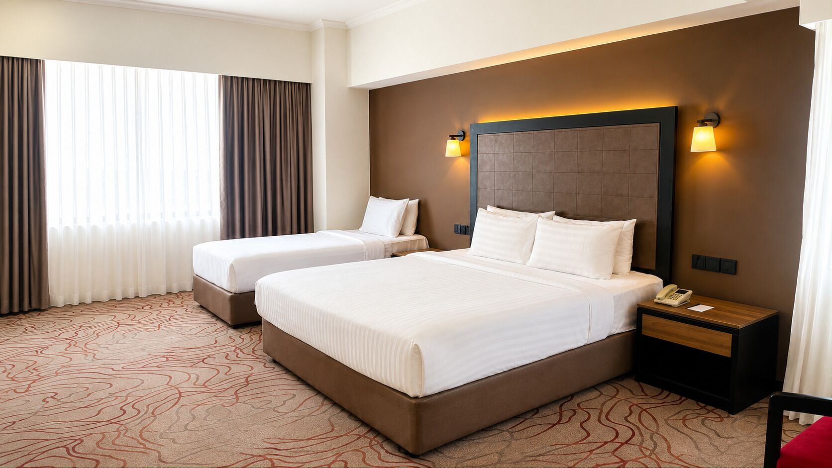 A hotel room with two beds, a nightstand with a phone, and a headboard with wall-mounted lights.