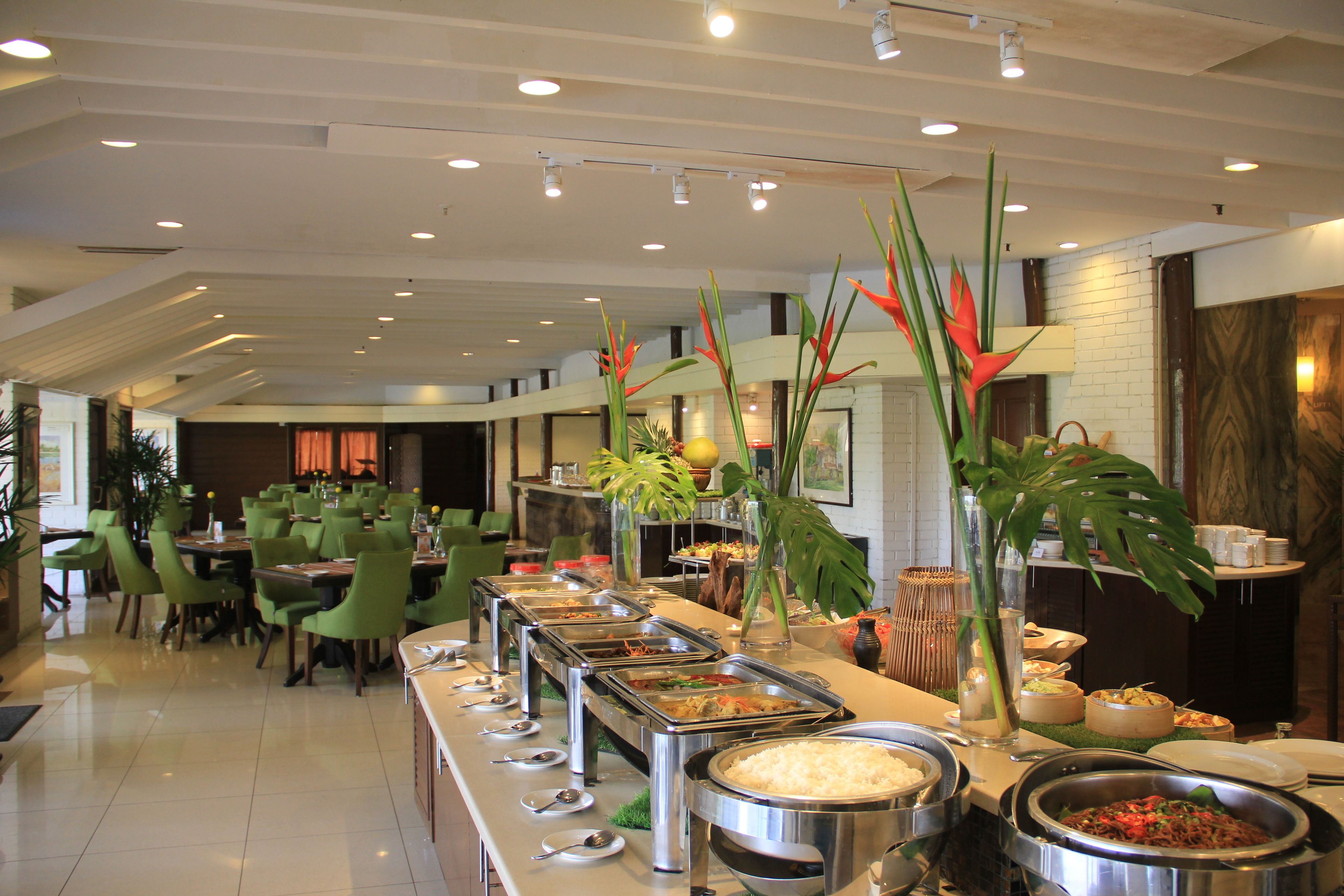 A buffet area with multiple food stations, green chairs, and potted plants.