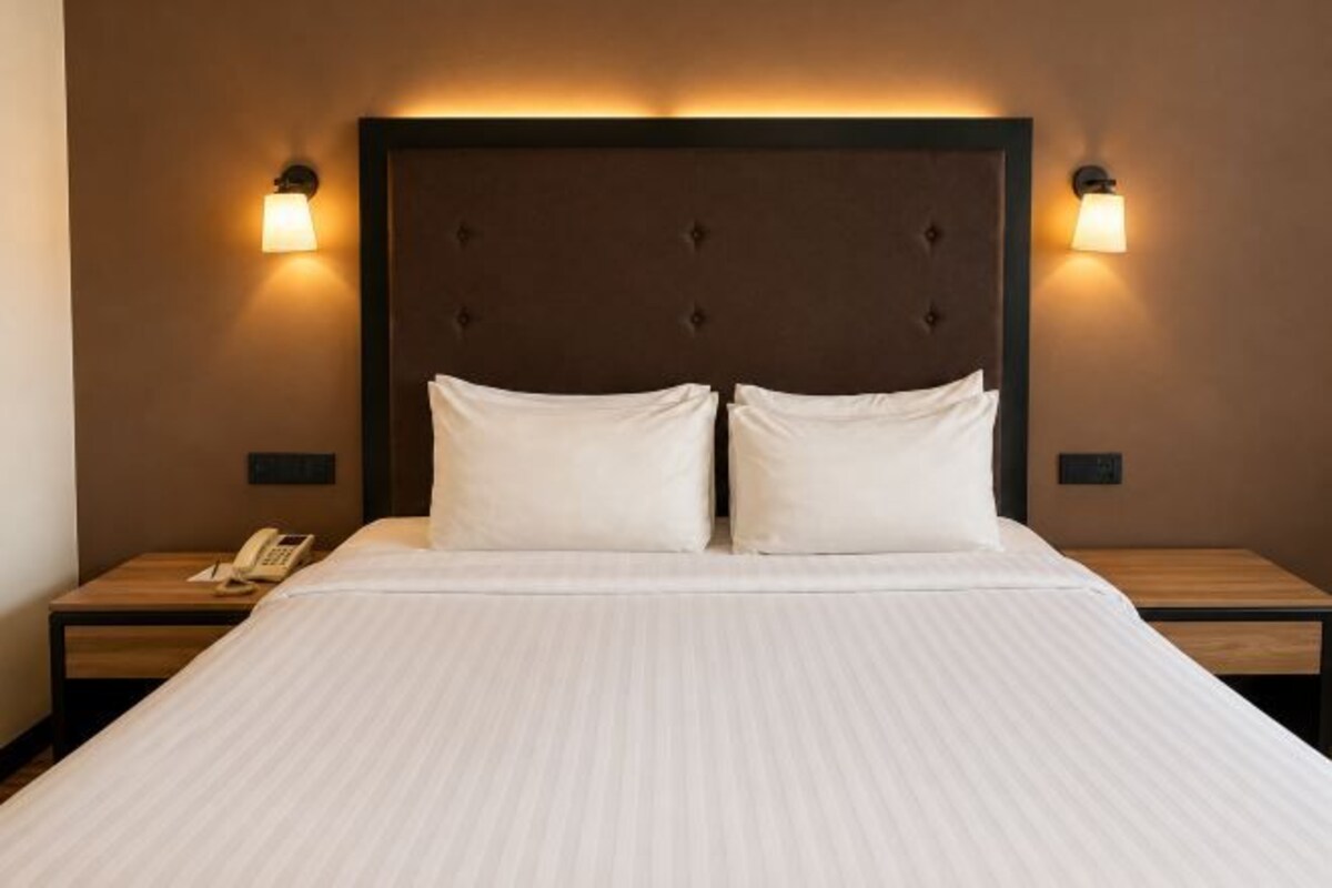 Habitación de hotel con una cama grande, dos mesitas de noche y lámparas fijadas a la pared.